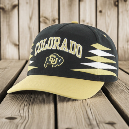 Black and yellow Colorado Buffaloes cap and logo on a wooden surface